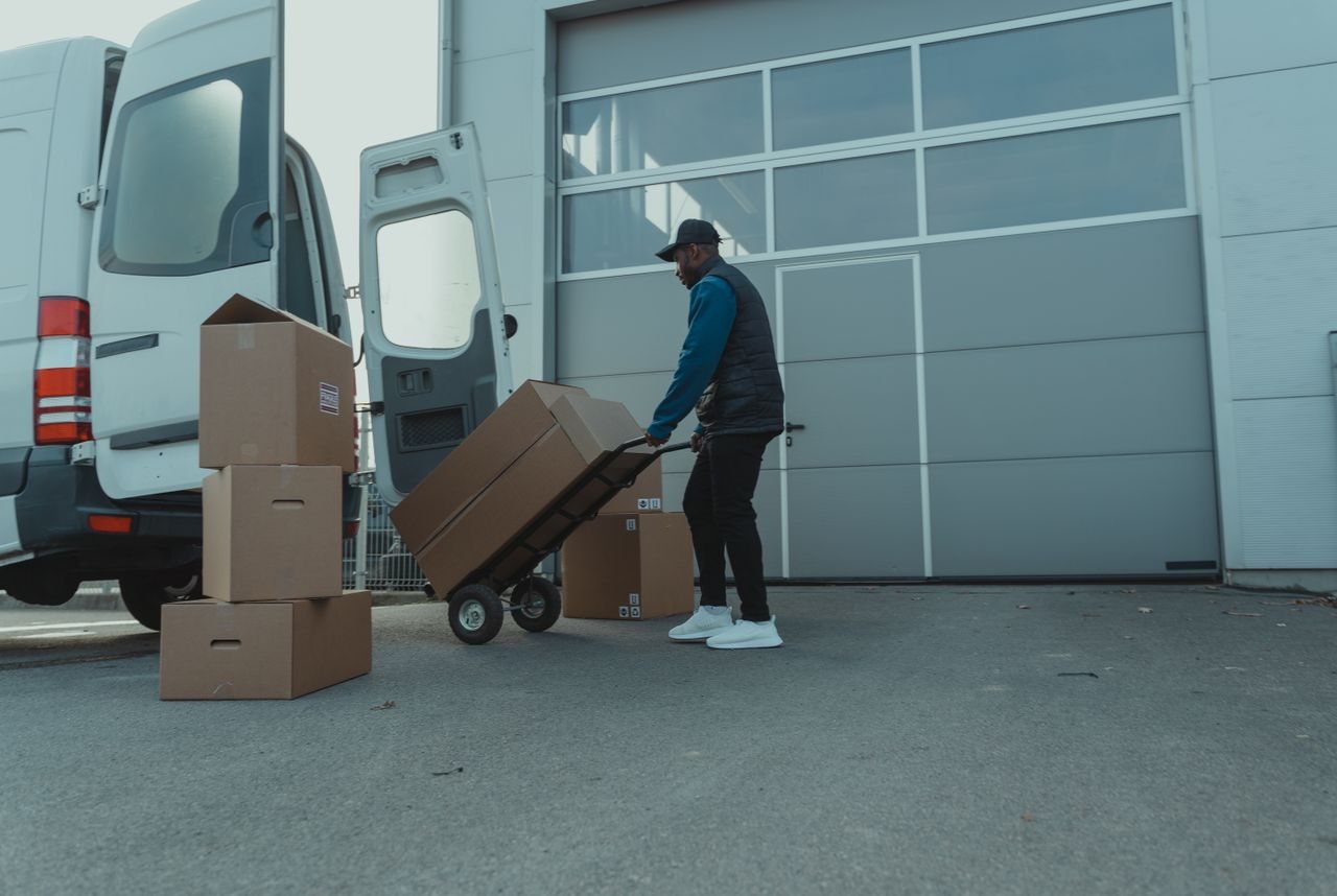 Free Courier unloading packages from a delivery van at a warehouse entrance. Efficient distribution. Stock Photo