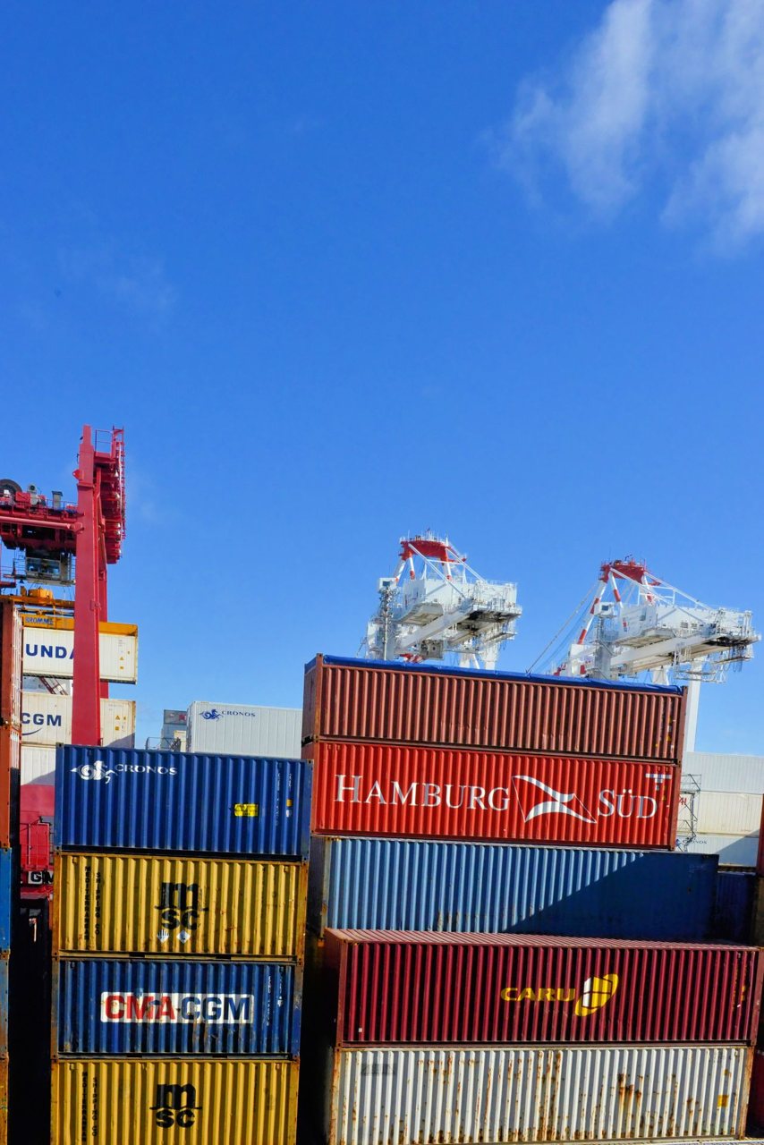 Free Colorful cargo containers stacked at a busy shipping port under a clear blue sky. Stock Photo