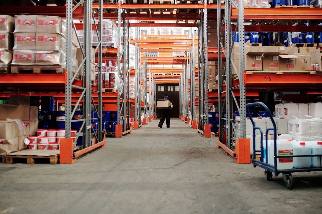 Free A worker carrying a box in a well-organized warehouse storage aisle. Stock Photo